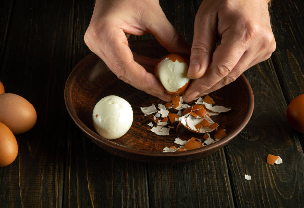 A cook peels a boiled egg from its shell on the kitchen table with his hands. Healthy eggs white diet concept. Advertising space.