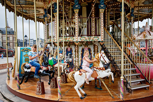 Adorable little girl and school kid boy having a ride on the old vintage merry-go-round in city of Honfleur France. Siblings, brother and small sister having fun