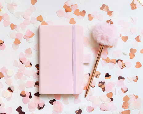 Pink hardcover notebook near hearts and fur pen on white table top view. Romantic girly mockup for Wedding, Valentines, Spring or Mothers day