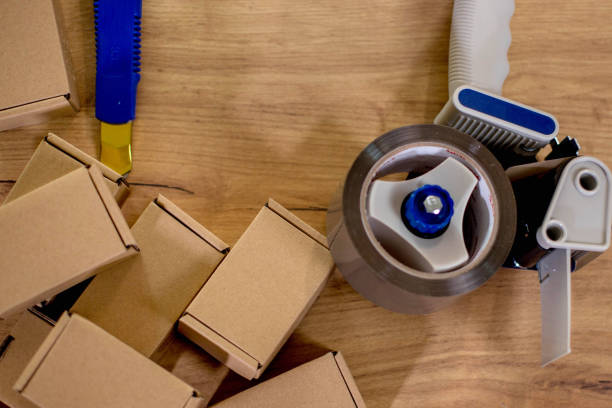 istock Composition with packing tape dispenser, laptop and paper boxes on composition of parcels 1954672266