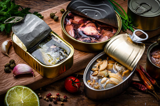 istock Three open tin cans with canned seafood shot on rustic wooden table 1954682137