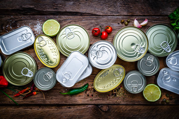 Overhead view of a group of canned food arranged side by side on wooden table Overhead view of a group of canned food arranged in a row on wooden table. High resolution 42Mp studio digital capture taken with Sony A7rII and Zeiss Batis 40mm F2.0 CF lens canned food stock pictures, royalty-free photos & images