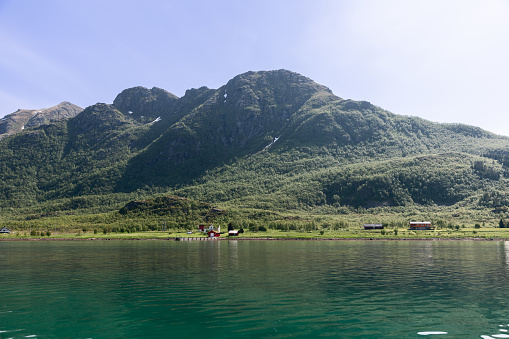 The serene emerald waters of a Norwegian fjord gently lap against the shores of a secluded farm, cradled by the towering green hills of Lofoten