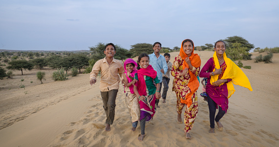 Group of happy Indian children running across sand dune - desert village, Thar Desert, Rajasthan, India.