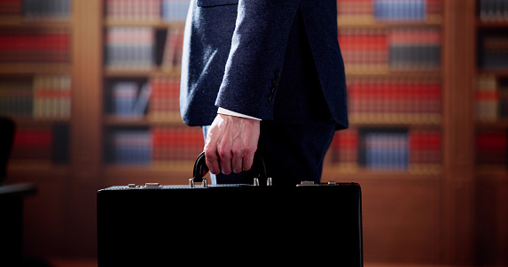 Midsection Of Lawyer Carrying Briefcase Against Bookshelf In Courtroom