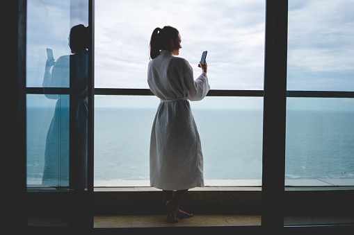 Woman wearing bathrobe standing on the hotel balcony with sea view