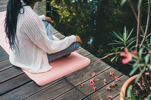 Woman sitting in lotus position on a yoga mat on a wooden pier by the lake. Relaxation activity concept.