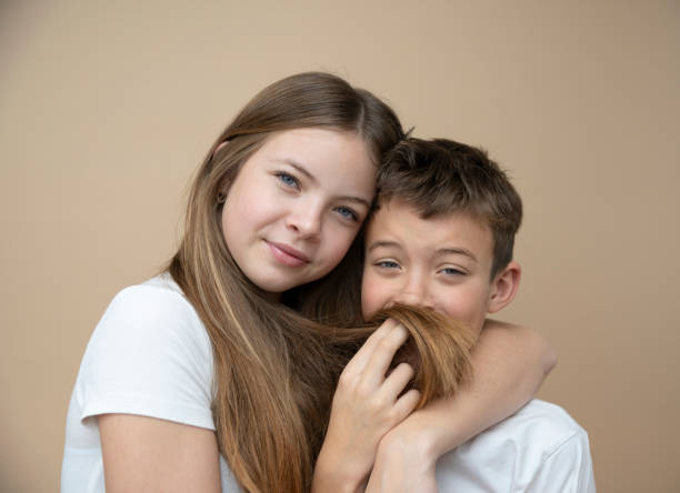 beautiful pretty 14 years old girl with her cute and cool 11 years old brother in front of brown background, brother and sister love - 10 11 years cheerful happiness fun - fotografias e filmes do acervo