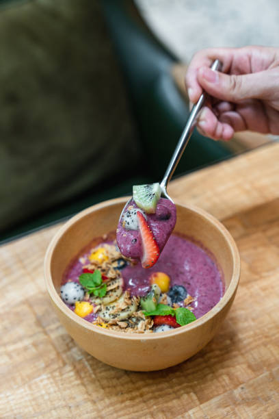 istock Spoon having fresh fruit yoghurt. Fruit and yoghurt bowl with cereals, kiwi, strawberries, mangoes, blueberries and dragon fruits on wooden table. 1954760902