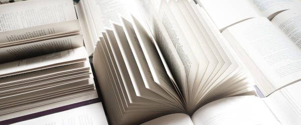 istock stack of books, close up. Open book on the table in library. Back to school concept. Open book on table with blur bookshelf background 1954764619