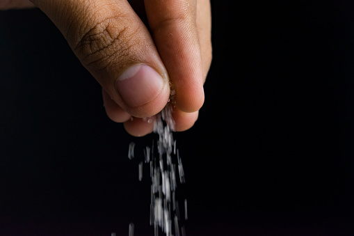 close up of man's hand sprinkling salt or sugar isolated on black background