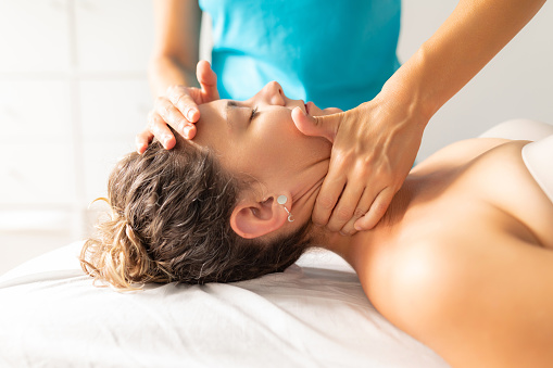 A physiotherapist performs a decontracting and relaxing massage on her patient's neck to relieve her of pain and tension