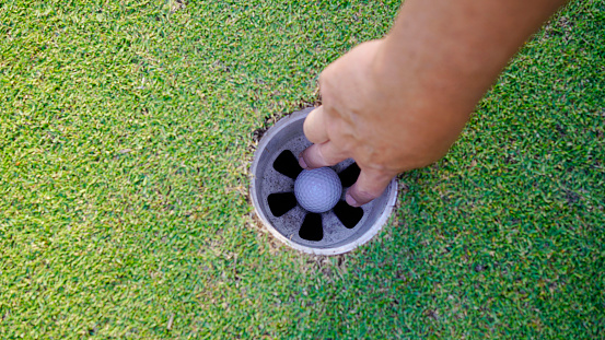 Top view of a golfer collecting golf balls in the hole after putting the ball into the hole after a match.