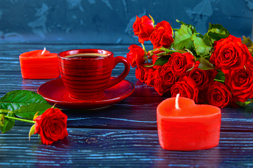 Red cup of coffee, candles in the form of heart, a bouquet of red roses. Romantic celebration of Valentine s Day.