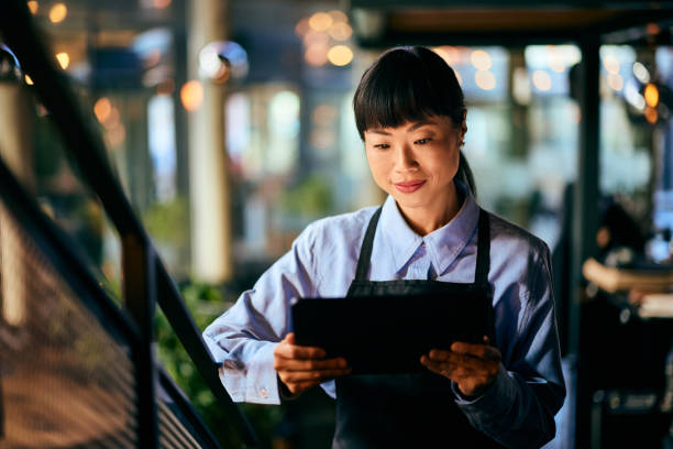 istock A focused Asian waitress, holding a digital menu, at the restaurant. 1954798752