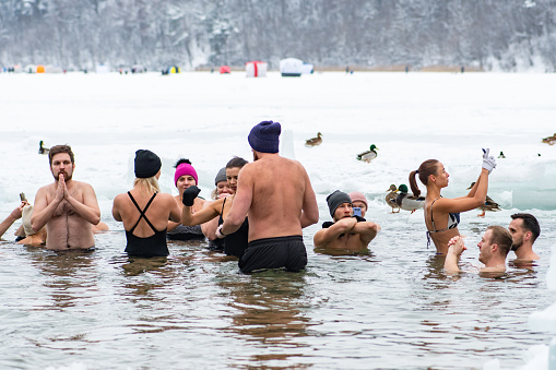 Vilnius, Lithuania - January 21 2024: Group of people ice bathing together in the freezing cold water of a frozen lake. Wim Hof Method, cold therapy, breathing techniques, yoga and meditation