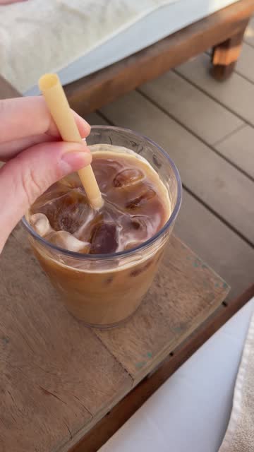 POV - woman drinking iced coffee by the pool. Woman mixing iced latte with a  straw