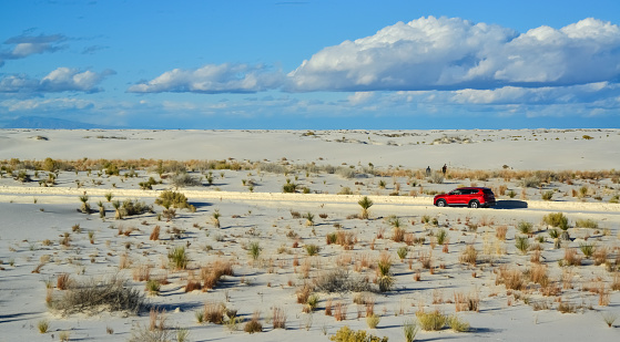 New Mexico, USA - November 23, 2019:  red car rides the harms of sand dunes from gypsum to White Sands National Monument, New Mexico, USA
