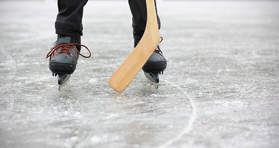 Ice skates and hockey stick close-up. Legs of a boy playing ice hockey on a frozen pond or in ice rink. Winter activities concept.