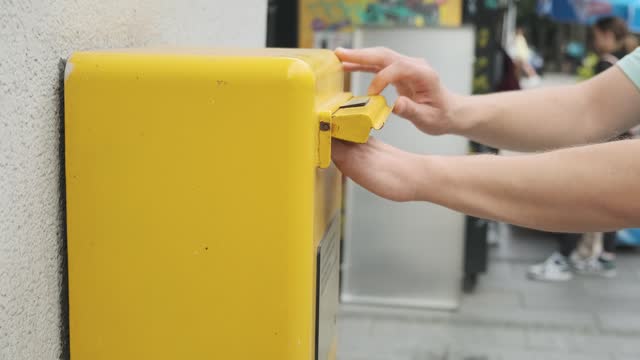 Male hand is drops a postcard in a yellow postbox. Man tourist sending post card and put it in yellow street mailbox