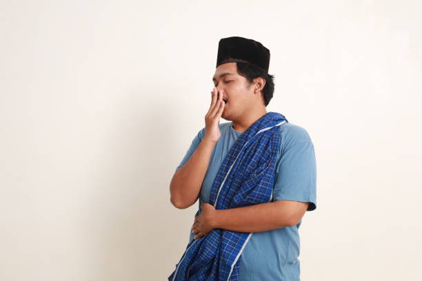 istock Sleepy young asian muslim boy with cap and scabbard standing while yawning 1954923944