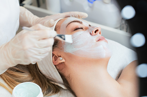 Beautiful and attractive young adult woman receiving professional beauty or skincare treatment with herbal clay mask. Modern and popular facial care treatment concept. Spa salon. High angle view.