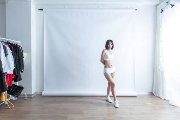 Asian female model with hands behind back in front of white background