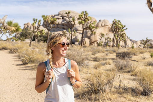 A cheerful young woman explores the breathtaking landscapes of Joshua Tree National Park while hiking, her joy evident in a radiant smile.