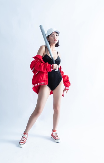 Asian woman in red bomber jacket and black swimsuit holding a baseball bat