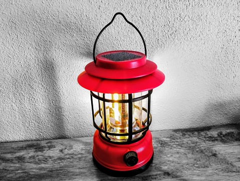 In the picture is a red lantern with a black steel frame and white clear glass. Inside are two small yellow and white light bulbs for lighting the tank. The lower part is red, the upper part is red as well, with ears. Carrying a black lantern h