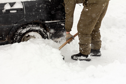 A man with a shovel in his hands removes snow around the car