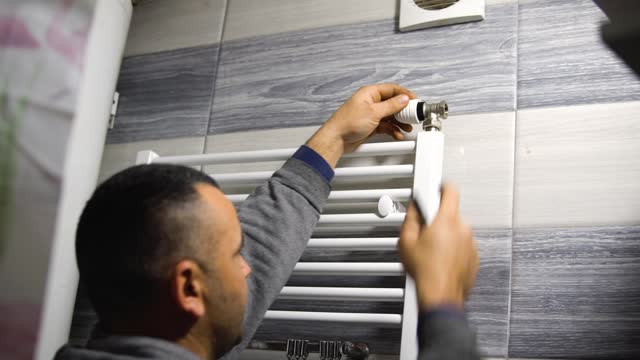 A plumber, a worker in uniform, is working, repairing a towel rail on the bathroom wall with a wrench. The concept of construction, maintenance and repair. stock video
