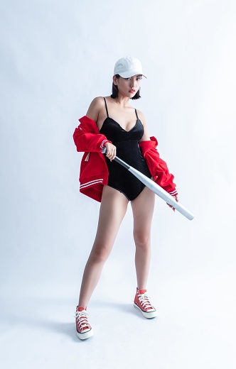 A woman in a red and white baseball jacket and black swimsuit holding a bat