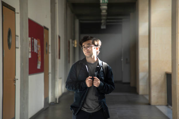 Young handsome bespectacled college student standing in university corridor