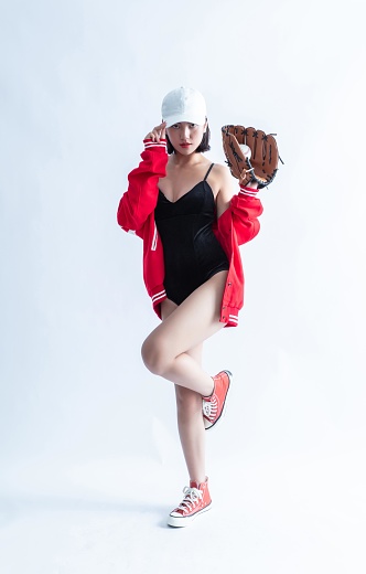 Asian woman in red bomber jacket and white cap posing with a baseball glove and a baseball