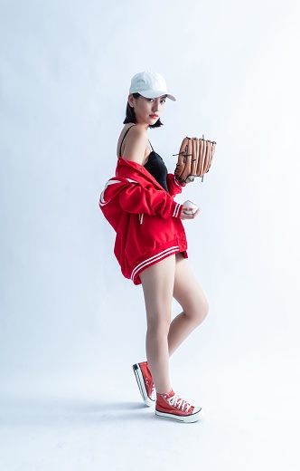 Asian woman in red bomber jacket holding baseball glove and ball