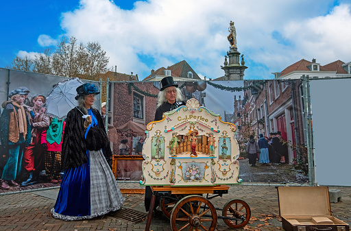 Deventer, Netherlands - December 16, 2023: Beautiful couple  in Victorian Style clothing at the barrel organ during the Dickens Festival More than 950 characters from the famous books of Charles Dickens relives in Deventer, Netherlands