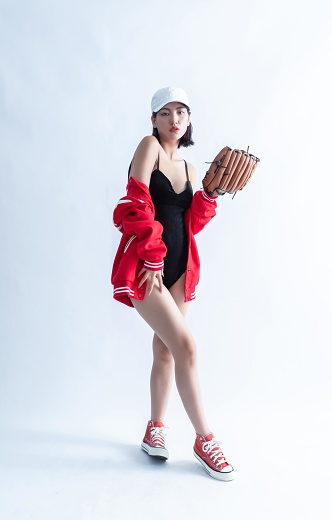 Asian woman in red bomber jacket and white cap posing with a baseball glove