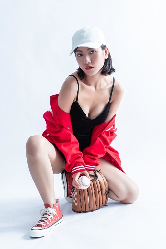 Asian woman in red jacket and white cap posing with baseball glove and ball