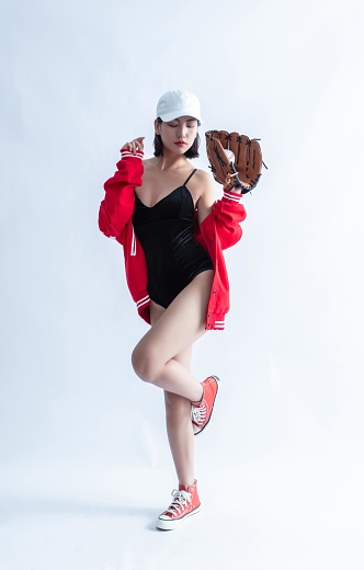 Asian woman in red baseball jacket and white cap posing with a baseball glove and a baseball