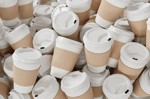 A heap of disposable white paper coffee cups with white lid and sleeves made from cardboard. Abundance of waste because of disposable containers.