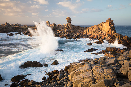 At sunset the waves of the rough sea break on the rocky coast.