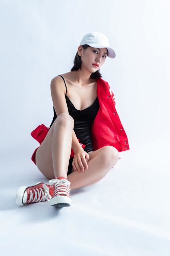 A Young Asian Woman Wearing a Red Bomber Jacket and a White Cap is Sitting on the Floor
