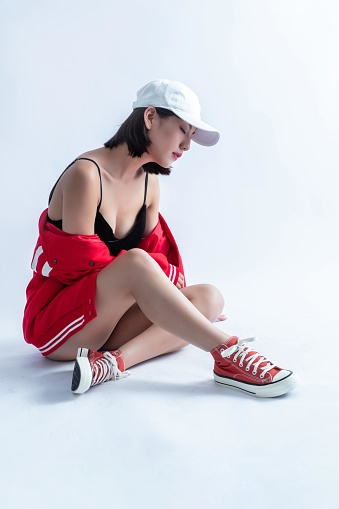 A Young Asian Woman Wearing a White Cap, Red Jacket, and Sneakers Sits on the Floor with Her Eyes Closed