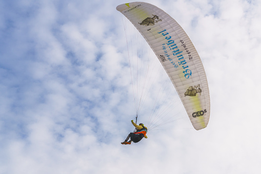 Person glides through the cloudy sky, attached to a colorful parachute, experiencing the joy of paragliding. Cloudy sky in the background, copy space