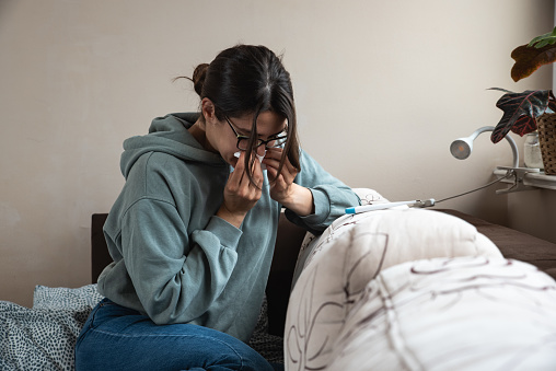 Young sick woman wrapped in a blanket wipes her nose with paper tissues, got sick because she didn't have money to pay for heating in her home or breakdown in the city heating network system.