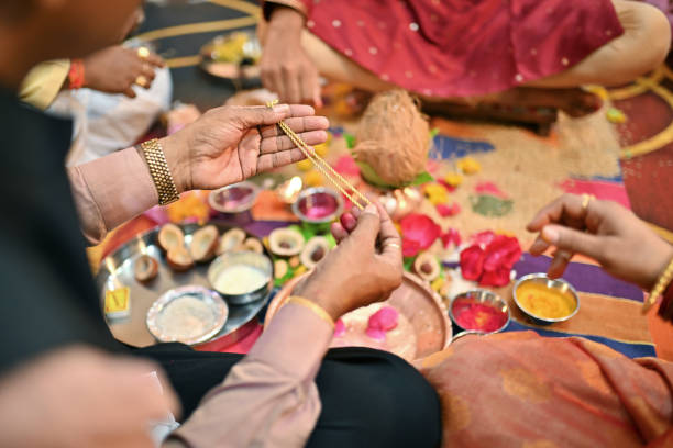 In this captivating photo, the cropped hand of a man is delicately holding a shimmering golden chain, an emblematic moment during a wedding ceremony.