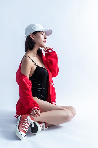 A Young Asian Woman Wearing a Red Bomber Jacket and White Cap Posing on a White Background