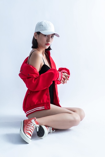 A woman wearing a red bomber jacket and a white cap is sitting on the floor