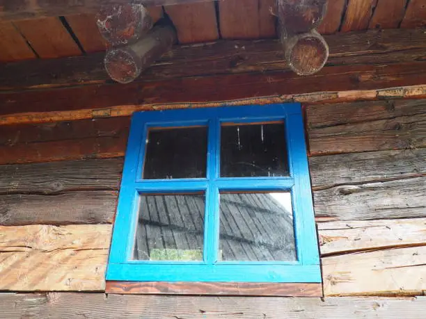 Ethno window with a blue wooden frame. Vintage house exterior. Architectural complex Stanisici. Log cabin. Izba building in rural wooded area on the territory of the settlement of the Eastern Slavs
